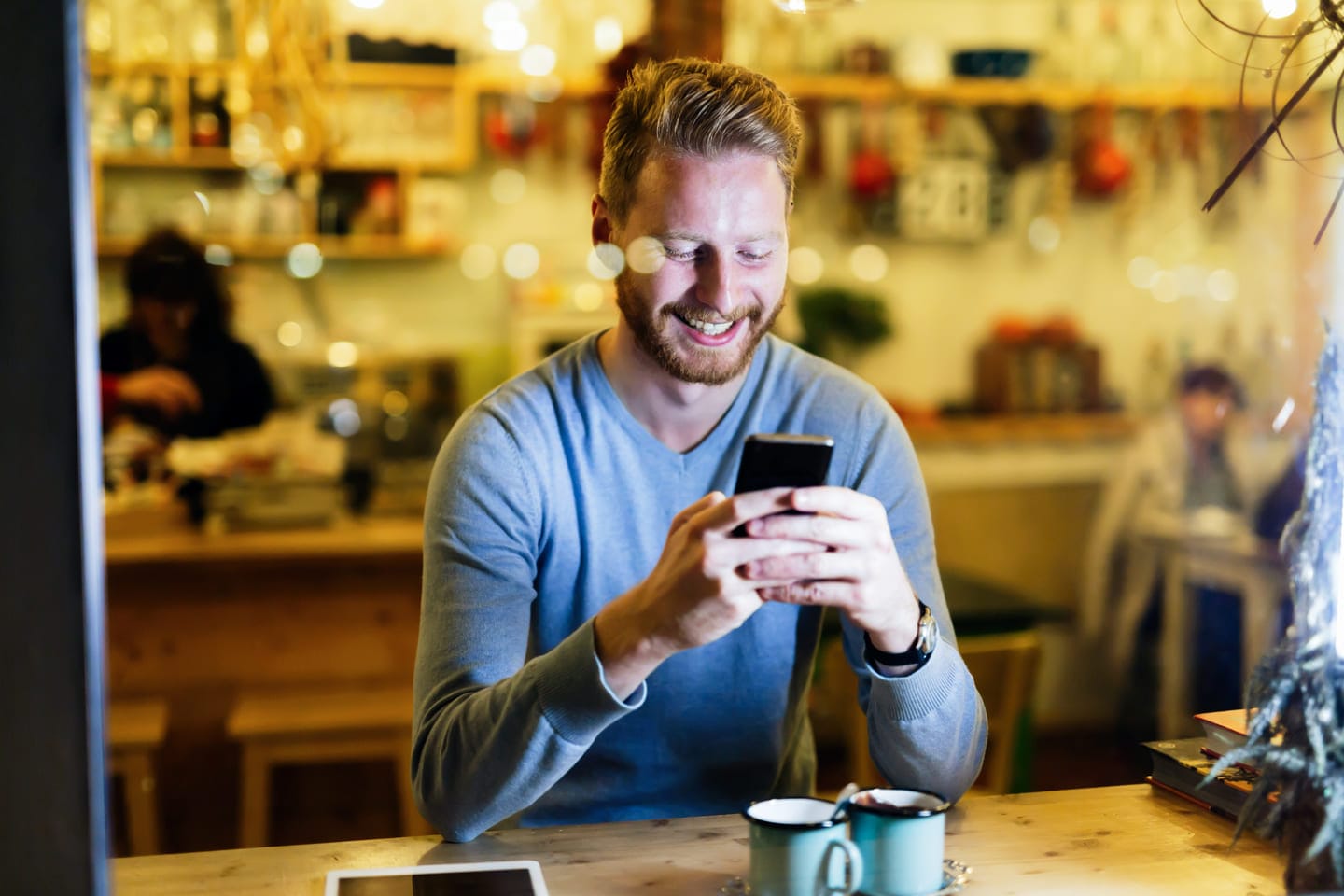 Mies tarkistaa puhelimella Rahalaitoksen lainatarjouksia kahvilassa