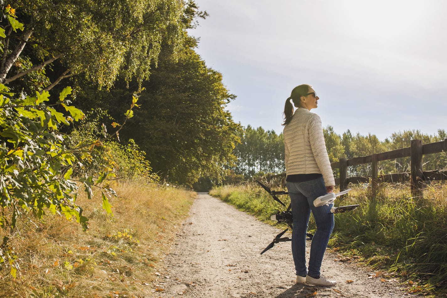 Nainen seisoo hiekkatiellä pitäen dronea kädessään, symboloiden uusia harrastuksia ja mahdollisuuksia, joita laina 20 000 euroa voi mahdollistaa