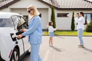 Paras sähkösopimus omakotitaloon 2026 Nainen lataa sähköautoa perheen kanssa omakotitalon pihassa