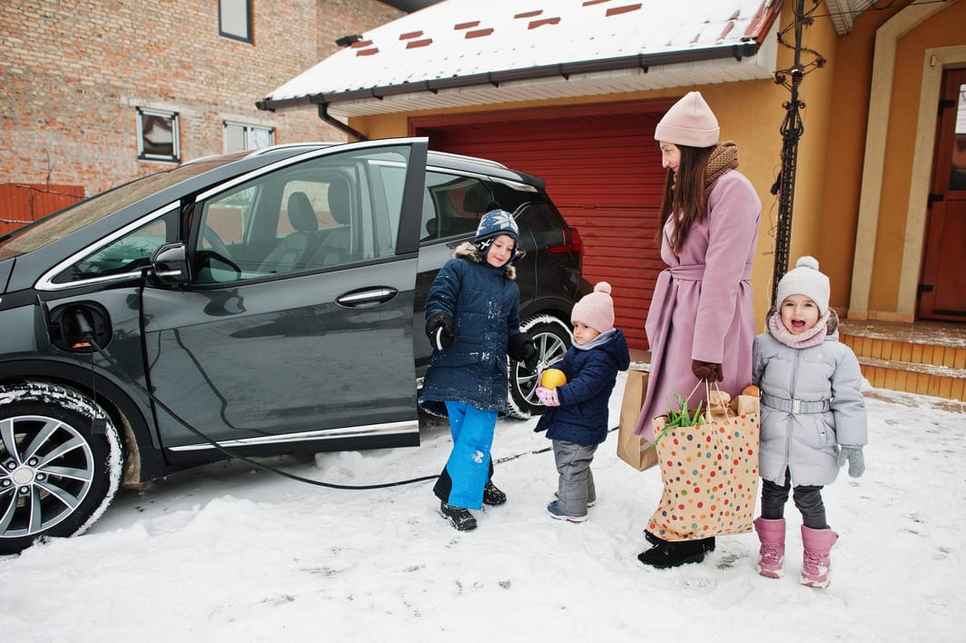 Nainen lataamassa sähköautoa lasten kanssa talvella