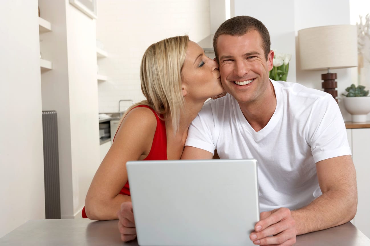 Nuori pari suunnittelee talouttaan tietokoneella keittiön pöydän ääressä